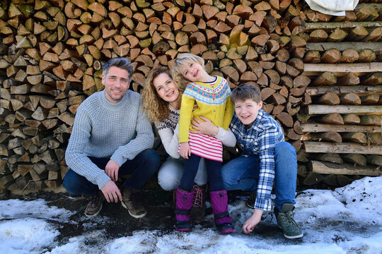 Portrait of happy family in front of stack of wood in winter