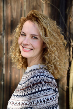 Blonde woman with curly hair smiling, norwegian sweater