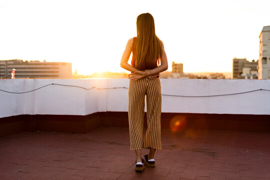 Rear view of teenage girl standing on roof terrace in the city at sunset