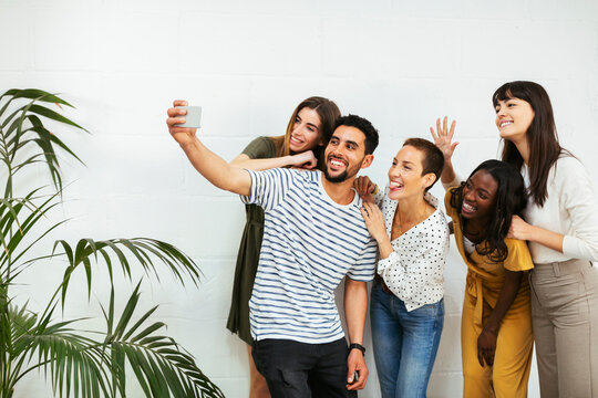 Playful colleagues standing at brick wall taking a selfie