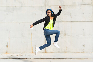 Woman with blue headphones listening music, jumping in the air