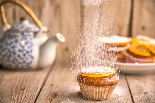 Sprinkling icing sugar on muffin with candied orange on top
