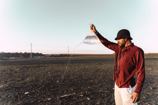 Young man holding plastic bag with water running out in barren land