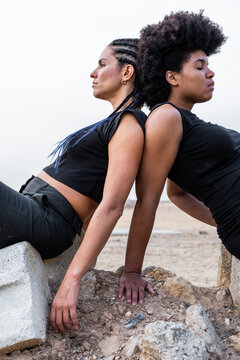Two women back to back on heap of rubble looking at distance