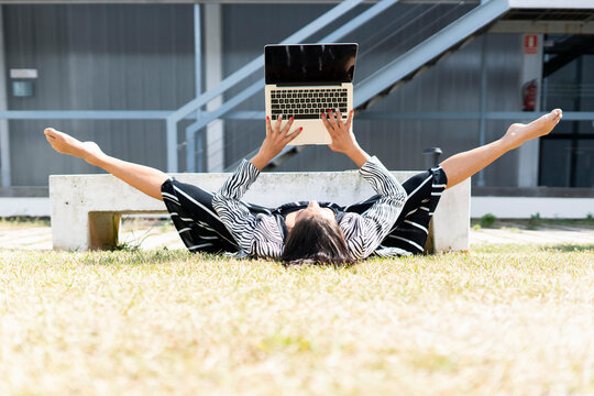 Female ballet dancer doing a spagat in front of an office, using laptop lying