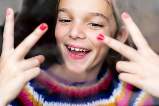Portrait of happy playful girl in striped pullover behind windowpane
