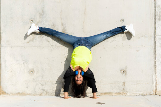 Woman with blue headphones listening music, making a handstand and split