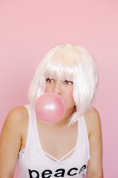 Portrait of young woman with pink gum bubble in front of pink background