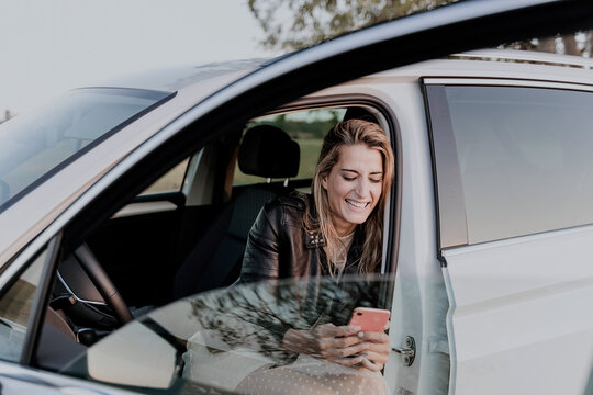 Blond woman using smartphone, sitting in white car