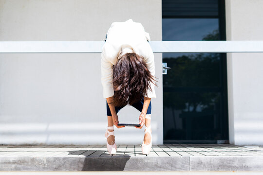 Female ballet dancer hanging over railing, holding tablet