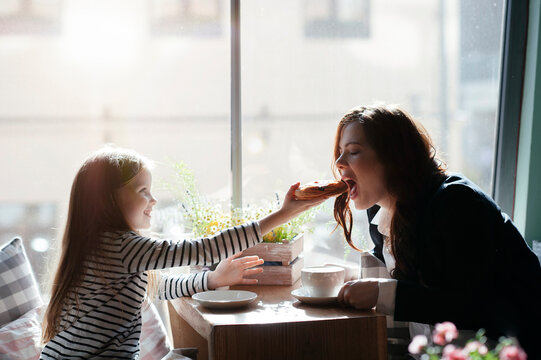 Smiling girl giving a peace of pie to her mother in cafe