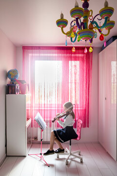 Girl sitting at the window at home playing violin