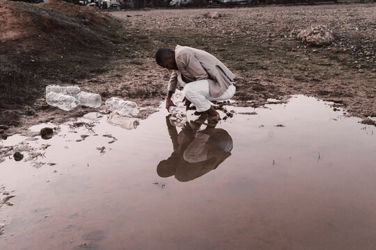 Young man filling plastic bottle with water at a water hole