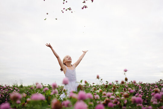 Girl standing in clover field, throwing flowers