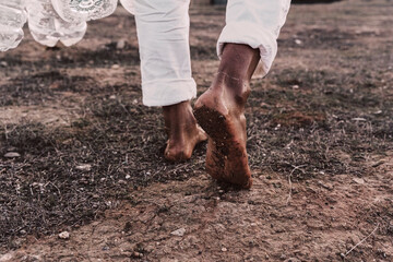 Close-up of man walking in barren land with empty plastic bottles