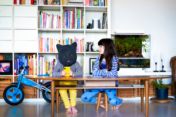Little girl watching sister, wearing cat mask, using smartphone