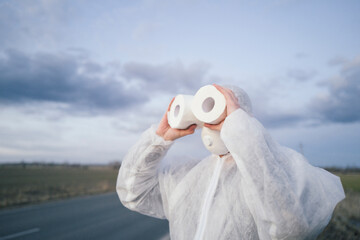 Man wearing protective suit and mask using toilet rolls like binoculars