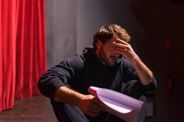 Rehearsing actor sitting on stage of theatre with script