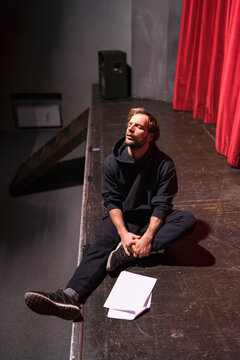 Rehearsing actor sitting on stage of theatre with script