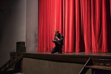 Actor crouching on stage of theatre studying script