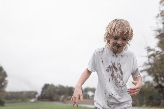 Portrait of blond boy with dirty face and t-shirt after jumping into a puddle