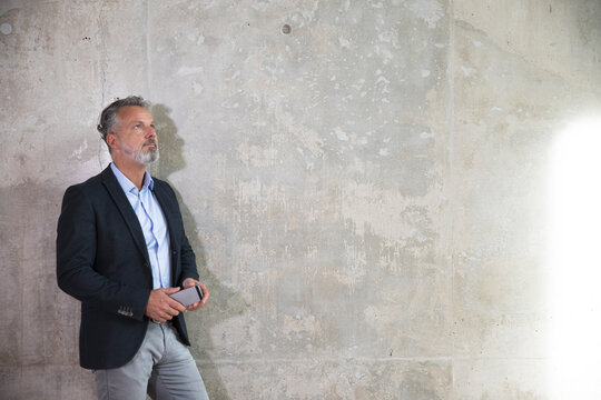 Businessman with cell phone leaning against concrete wall