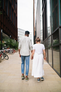 Back view of young couple walking hand in hand on pavement