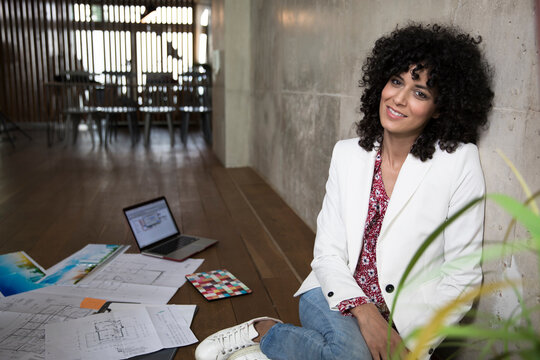 Portrait of smiling businesswoman sitting on the floor in a loft surrounded by documents