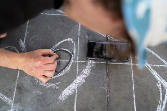 Street art, pavement artist drawing an eye on pavement and using smartphone