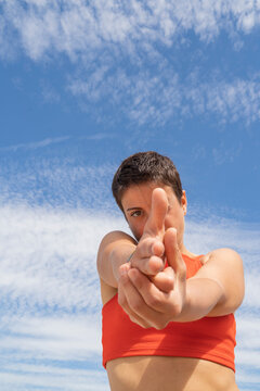 Woman making shooting gesture with her hand in front of sky