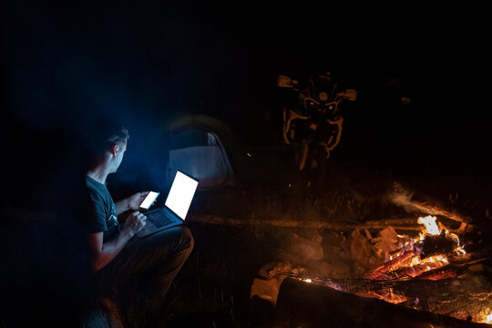 Man using laptop and smartphone at the fireplace at night