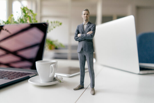 Businessman figurine standing on a desk with mobile devices and a cup of coffee