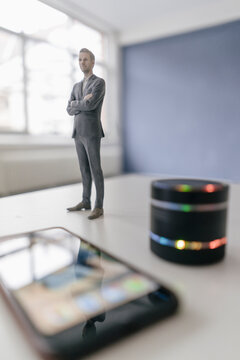 Miniature businessman figurine standing next to smart home loudspeaker and smartphone
