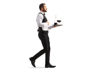 Full length profile shot of a waiter carrying a red wine decanter on a silver tray and walking