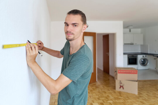 Young man measuring the wall in an empty apartment