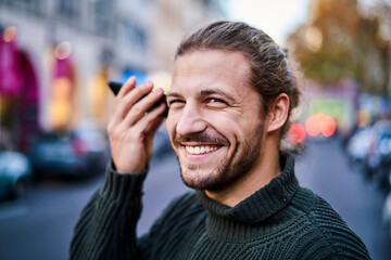 Portrait of laughing young man using smartphone on the street in the evening