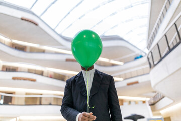 Mature businessman hiding face behind green balloon