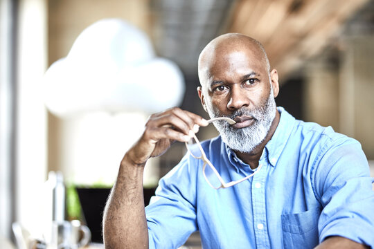 Mature businessman in office thinking with cloud balloon in background