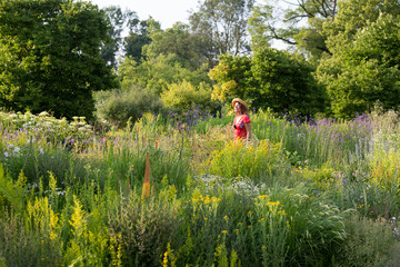 Woman wearing straw hat and red summer dress in garden with wildflowers