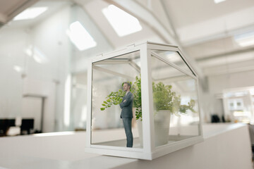 Businessman figurine standing in glasshouse with plant