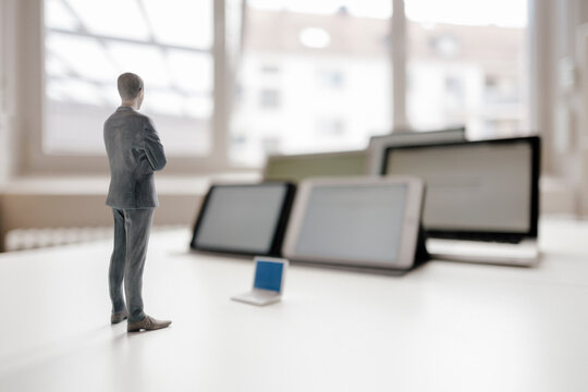Businessman figurine standing on desk, facing mobile devices