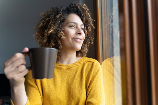 Woman sitting at window, taking a break, drinking coffee