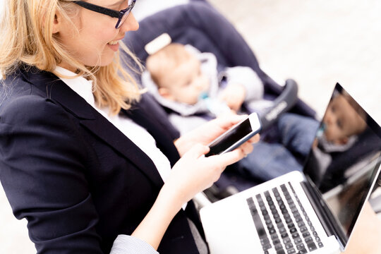 Young businesswoman with baby boy in stroller working outdoors