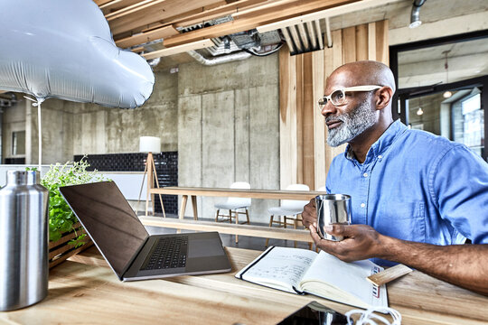 Mature businessman sitting at table in modern office with cloud balloon and laptop
