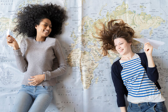 Friends lying on map, throwing paper palnes, planning their vacations
