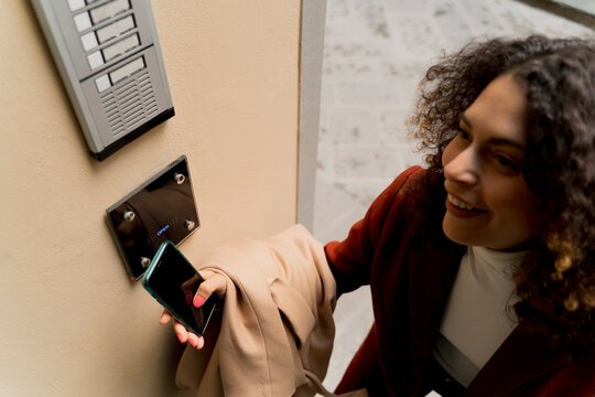 Smiling woman opening door with smartphone