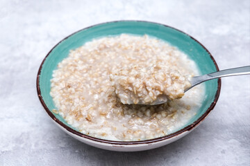 A spoon of cooked oats porridge above a green bowl, healthy breakfast and dieting product close up, tasty vegan food