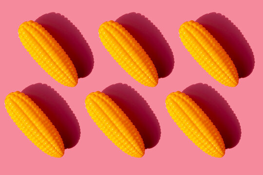 Studio shot of six plastic corn cobs against pink background