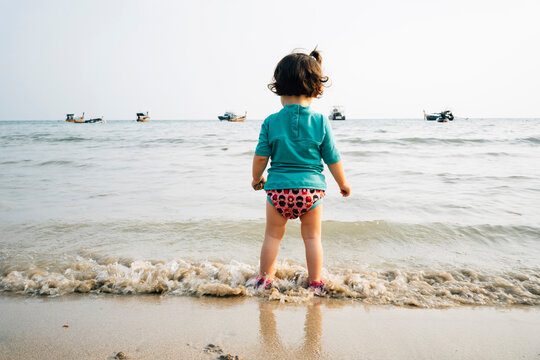 Thailand, Koh Lanta, back view of baby girl wearing UV protection shirt standing at seashore