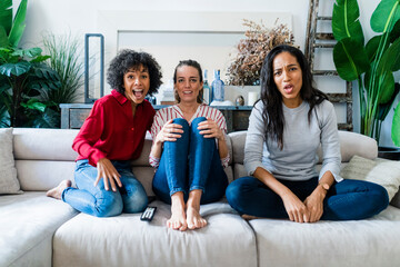 Three excited women on couch at home watching Tv